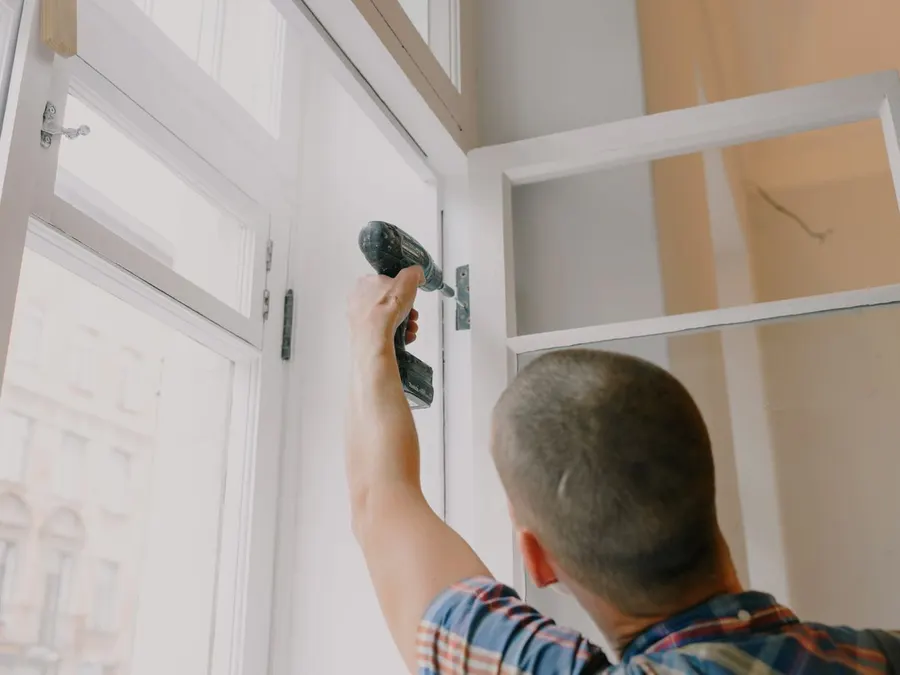 A tradesperson uses a cordless screwdriver to install hinge hardware on a door frame