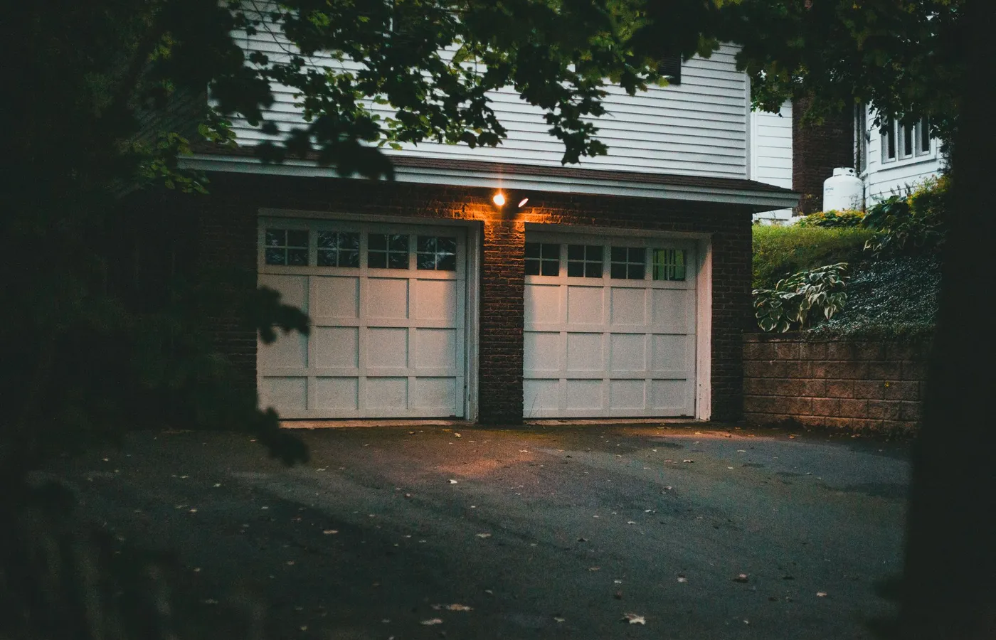 A white raised-panel double garage door on a home, lit by evening porch light